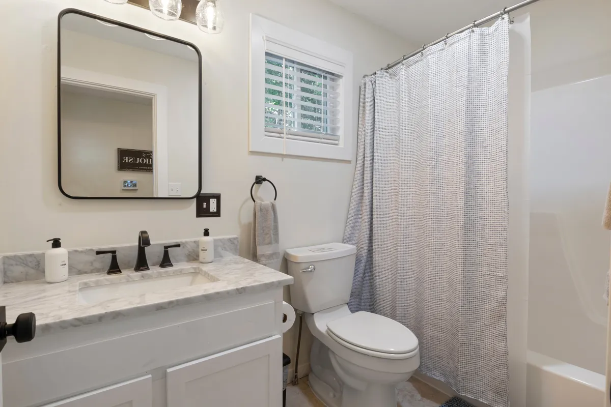 A serene bathroom with a marble-topped vanity, a well-lit mirror, a shower curtain, and a toilet, all in a calming atmosphere. The space suggests modern convenience, privacy, and opportunities for relaxation and self-care.
