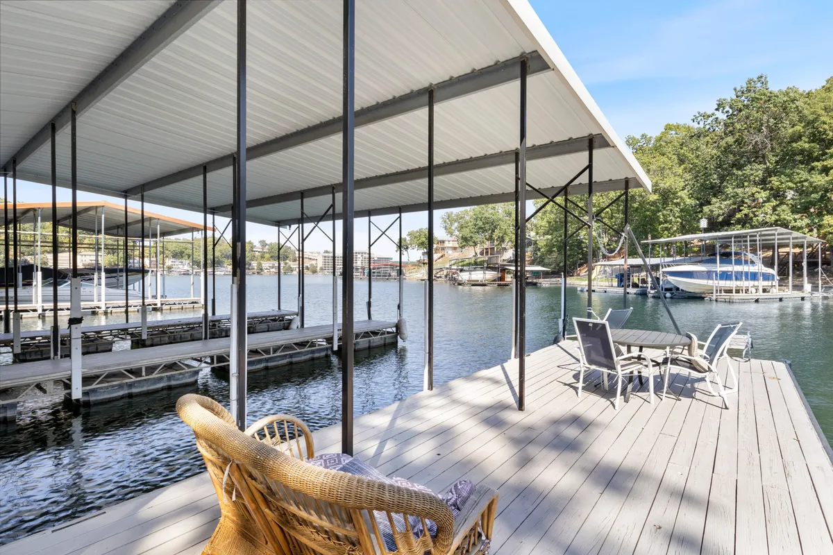 A dock stretches out over the lake, with boats moored alongside and a dedicated seating area at the end of the dock. The calm waters and warm evening light set a tranquil mood, inviting both sunbathing and gathering for sunset views.
