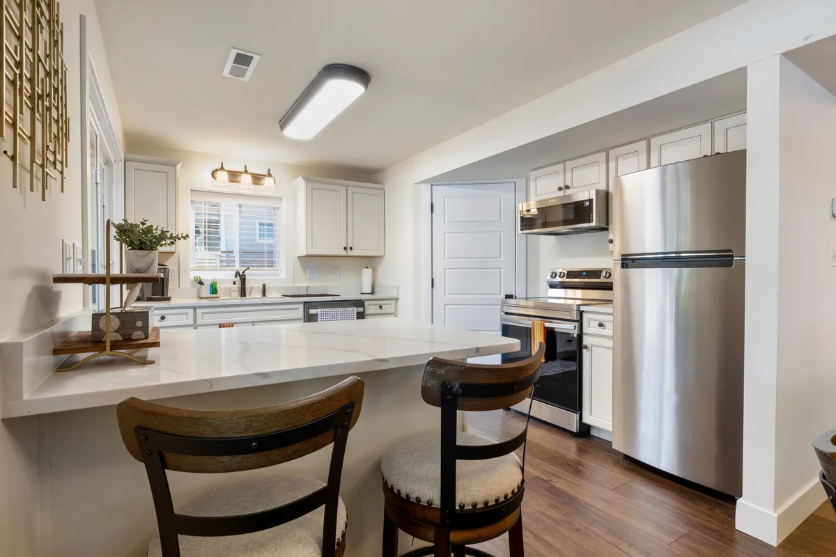 A functional, modern kitchen with a central island, seating, stainless steel appliances, and ample cabinetry. Natural light pours in through the window, illuminating the workspace.