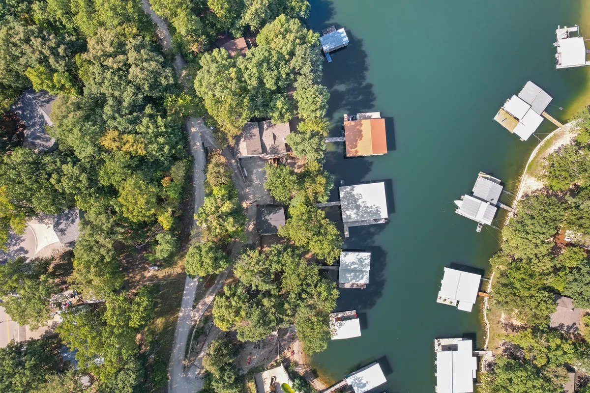 A picturesque view of houses nestled among lush trees, several docks extending into the lake, and a meandering road that invites exploration. The image conveys a broader sense of the lakeside community and the outdoor spaces waiting to be discovered, inviting families to explore more beyond the property.