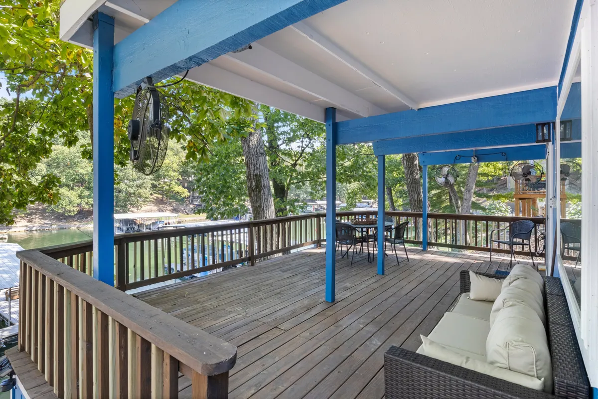 A spacious deck with comfortable outdoor seating and a dining table overlooks serene waters, surrounded by trees. The area is set up for outdoor meals, relaxation, and soaking in panoramic lake views. The setting captures the essence of shared family time and al fresco dining in a scenic environment.