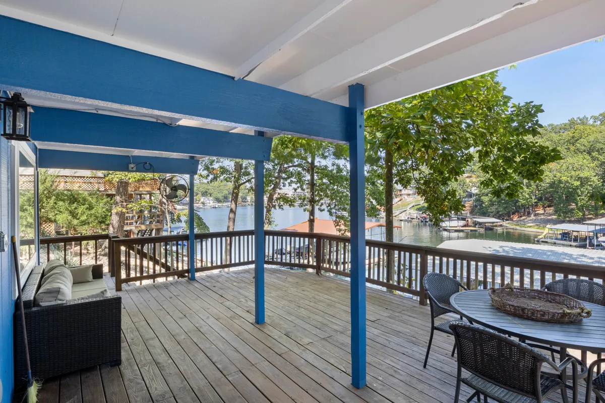 This image features a wooden upper deck with blue beams and a seating area looking out over the lake. The inviting space is designed for relaxing, dining, or stargazing, with an unobstructed view of the water and sky.
