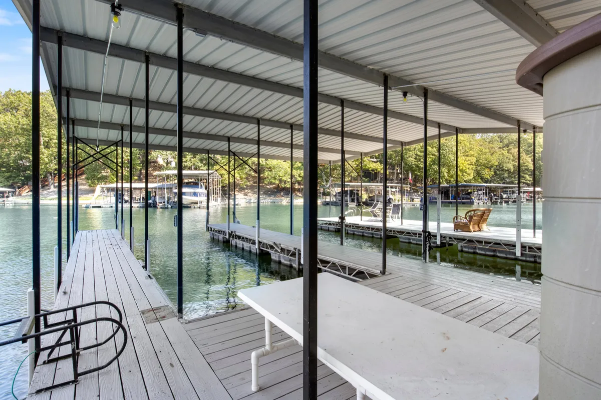 A serene lakeside scene showing docks extending over calm water, boats ready for use, and lush trees surrounding the area. The ambiance is tranquil, perfect for relaxing, socializing, and enjoying the water's edge as the sun sets.