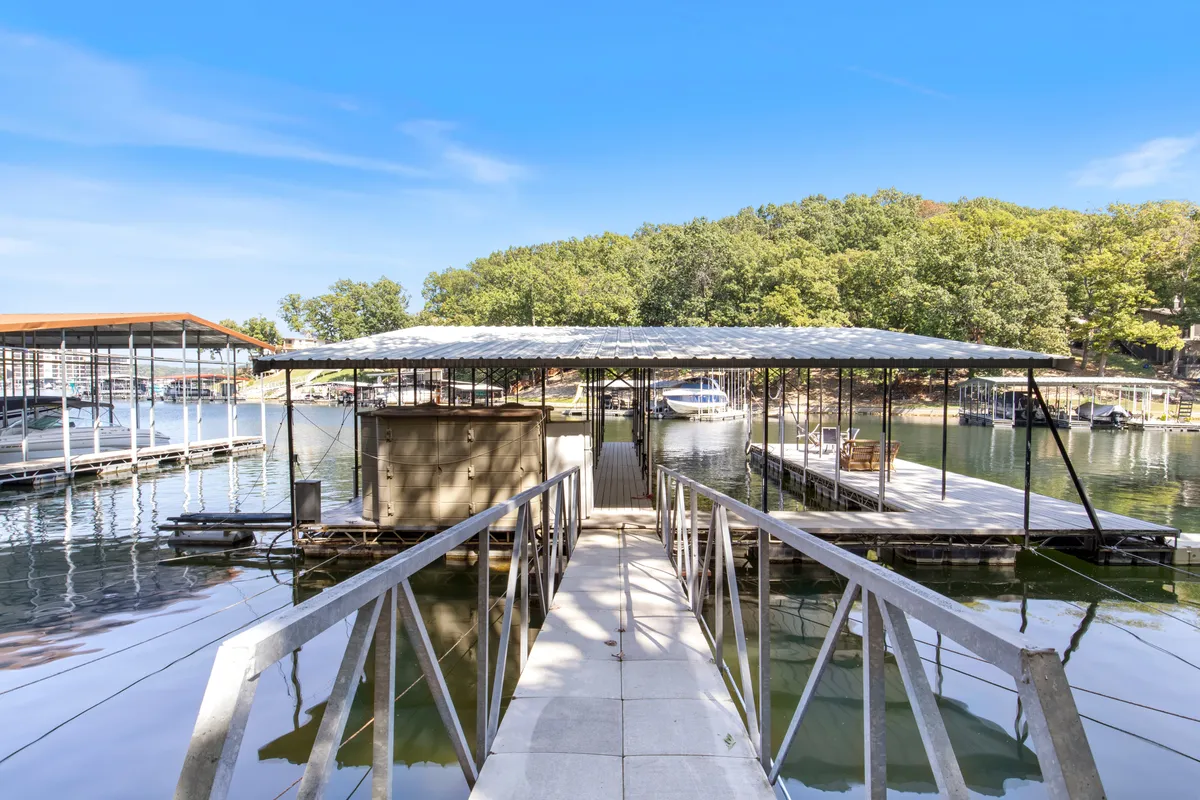 A sunlit dock stretches over calm lake waters, framed by leafy trees and a few boats tied up along the edge. The inviting space is perfect for fishing, swimming, or simply relaxing by the water. The scene exudes tranquility and outdoor adventure, with the dock providing direct access to the lake.