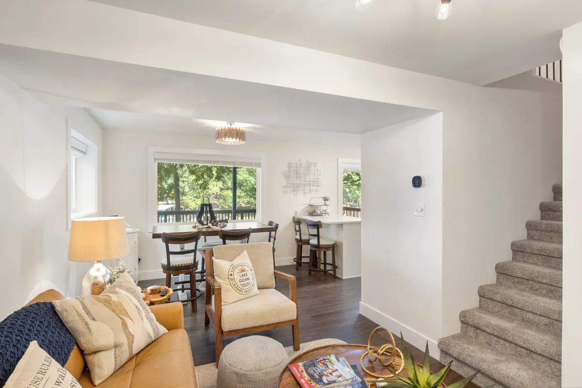 This image features a welcoming open-plan interior where a cozy sofa sits adjacent to a sizable dining table, with a staircase in view. The space is clearly arranged to foster gathering, relaxation, and entertaining, emphasizing togetherness. The inviting layout suggests shared activities like family game nights or group meals.
