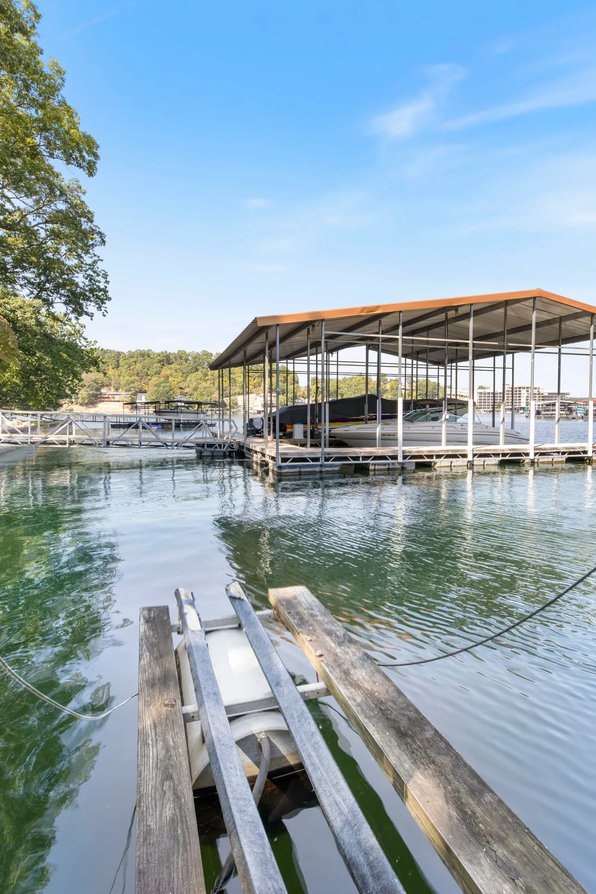A boat dock with sheltered slips sits on glassy water under a vibrant blue sky. Several boats are moored, and the calm ambiance evokes leisurely afternoons spent fishing or prepping for lake adventures.