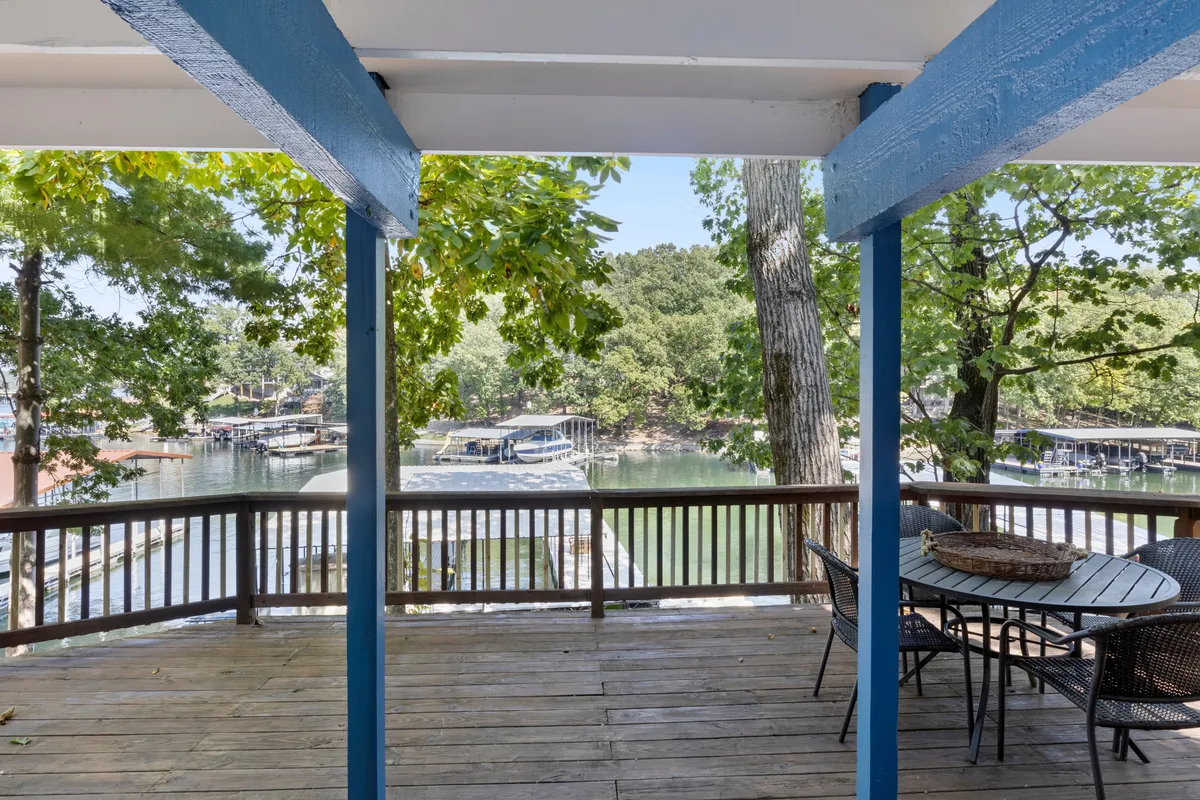 This exterior image features a spacious wooden deck with a dining table, surrounded by trees and overlooking the water. The setting is serene and inviting, ideal for outdoor dining, family gatherings, or simply relaxing and taking in the view.
